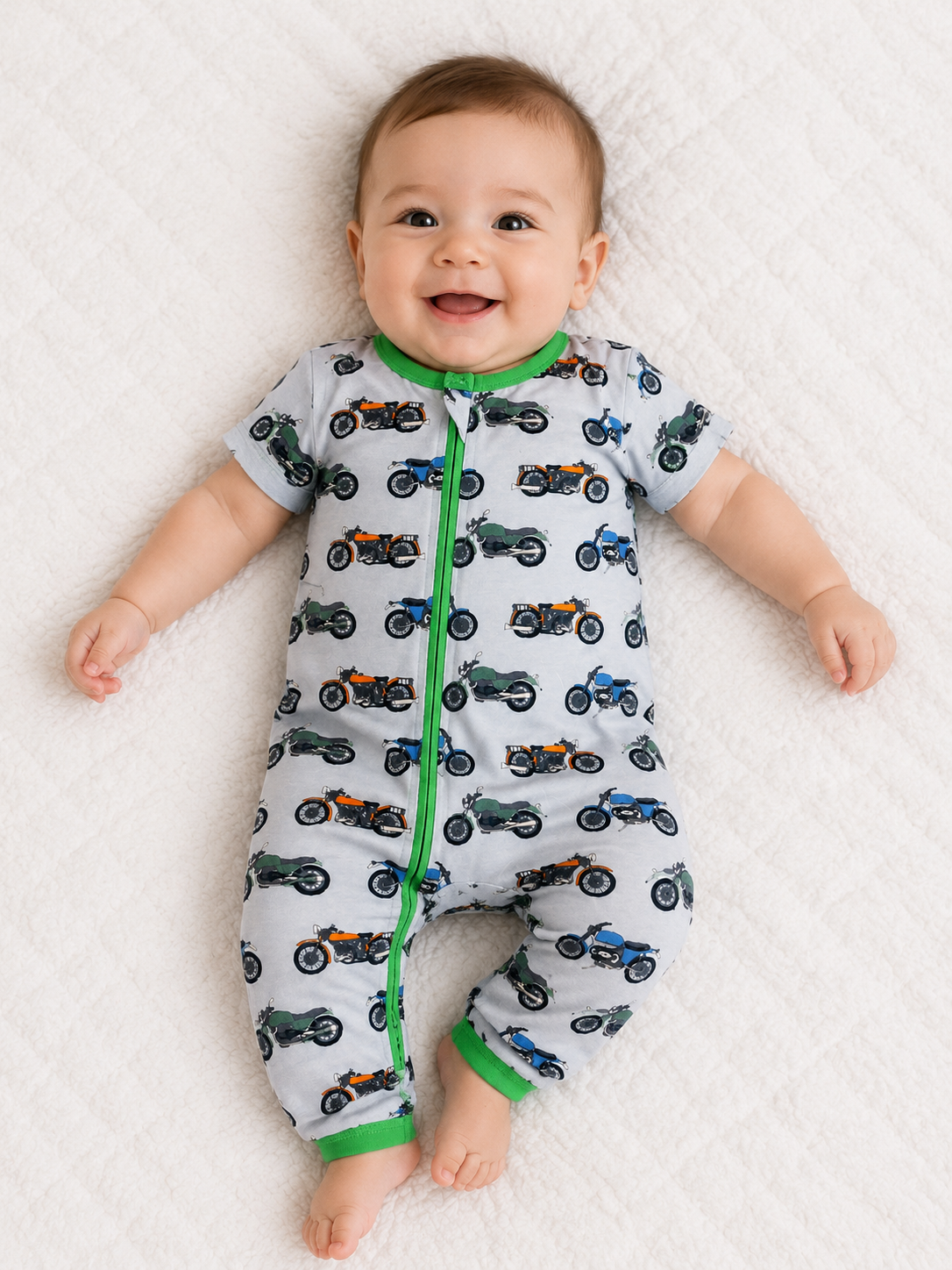 Baby wearing a onesie with motorcycle patterns laying on a white blanket romper made from bamboo fabric