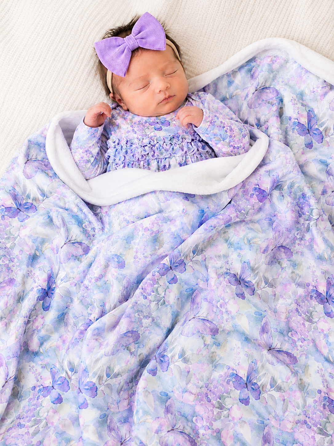 Newborn baby wrapped in a purple butterfly blanket with a matching bow.