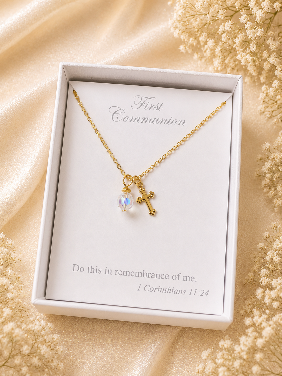 Gold necklace with a cross and pearl pendant in a white box on a beige fabric background