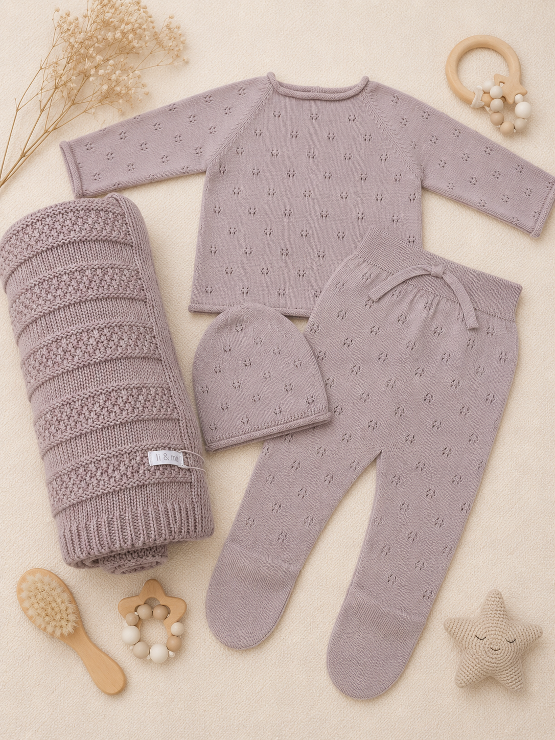 Baby clothing set with mauve outfit, hat, and blanket on a beige background