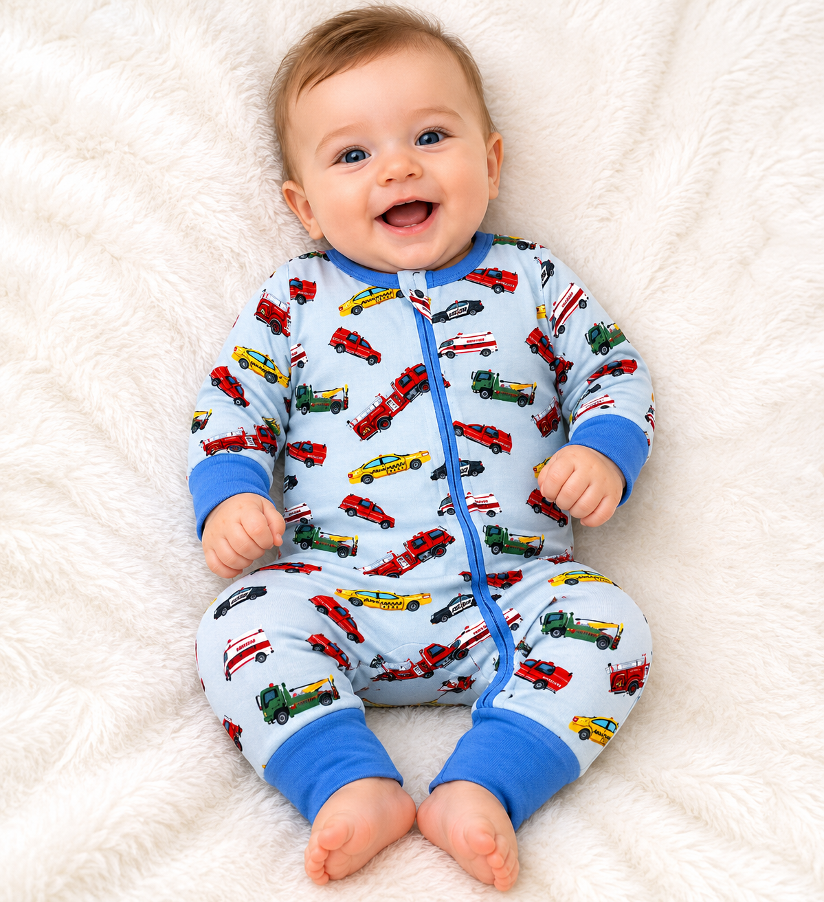 Baby wearing a colorful pajama with vehicle patterns made from bamboo fabric on a white fluffy blanket