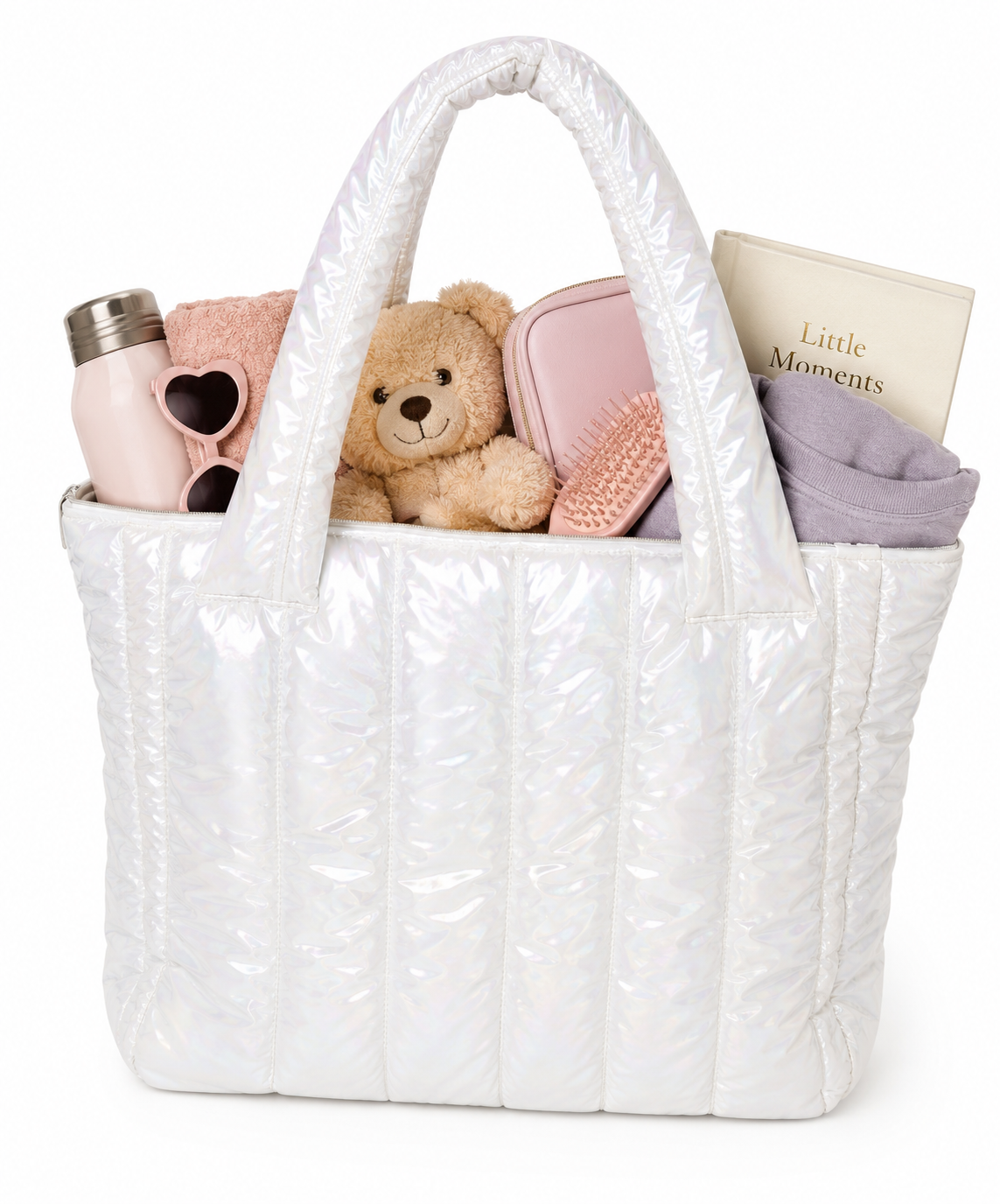 A white quilted puffy tote bag filled with baby essentials including a pink bottle, teddy bear, pink accessories, and a book on a white background.