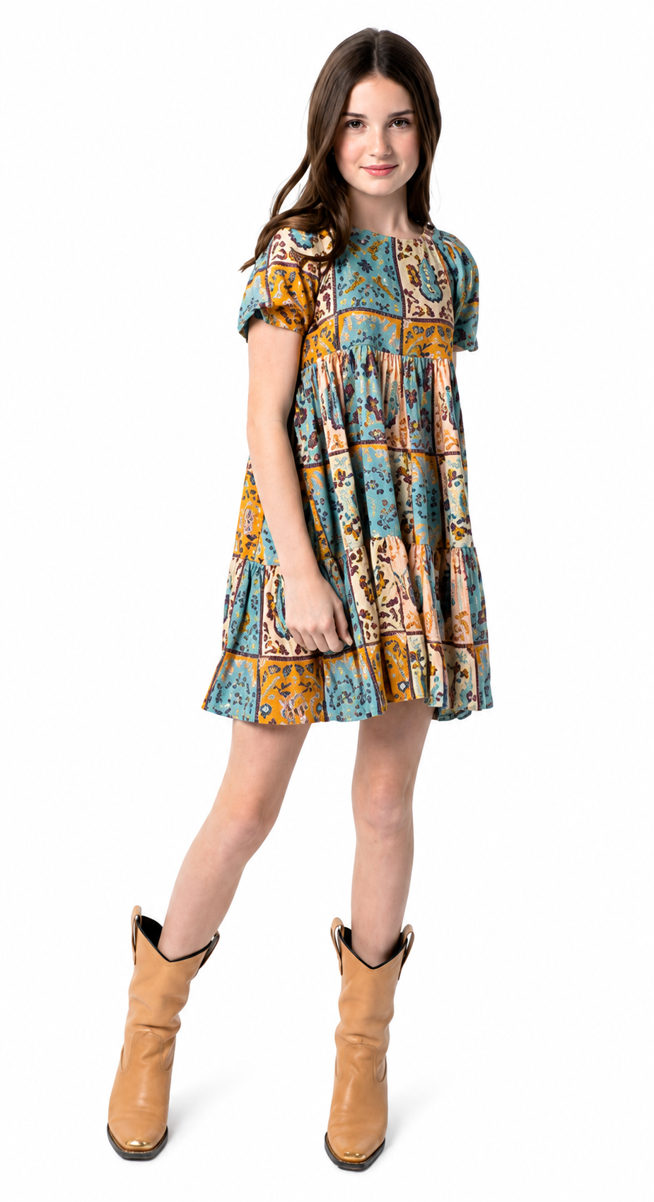 A young girl modeling a short-sleeve tiered dress with a colorful patchwork print in blue, yellow, and brown, paired with tan cowboy boots, against a plain white background.