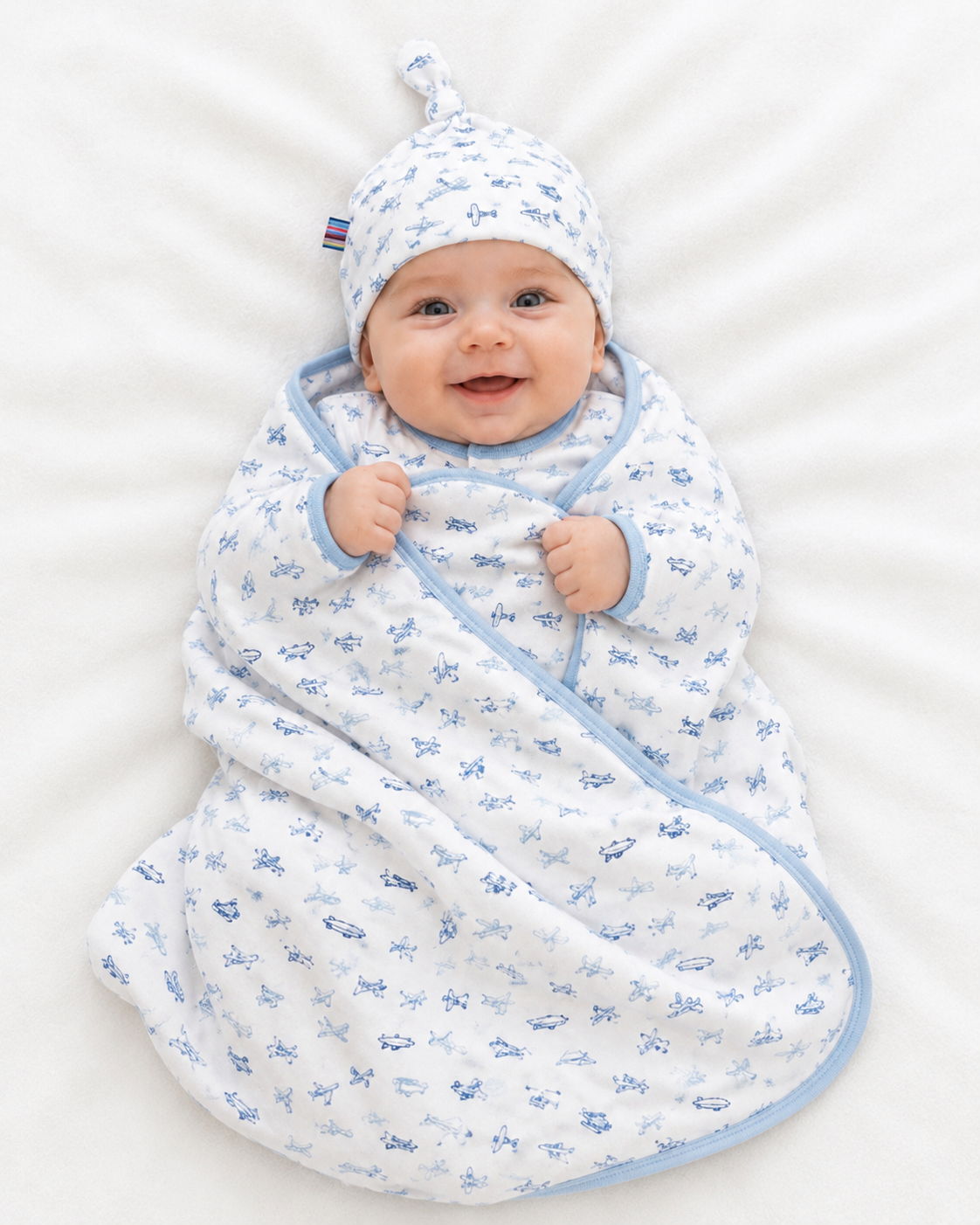 Baby wrapped in a blue and white airplane patterned swaddle with matching hat on a white background