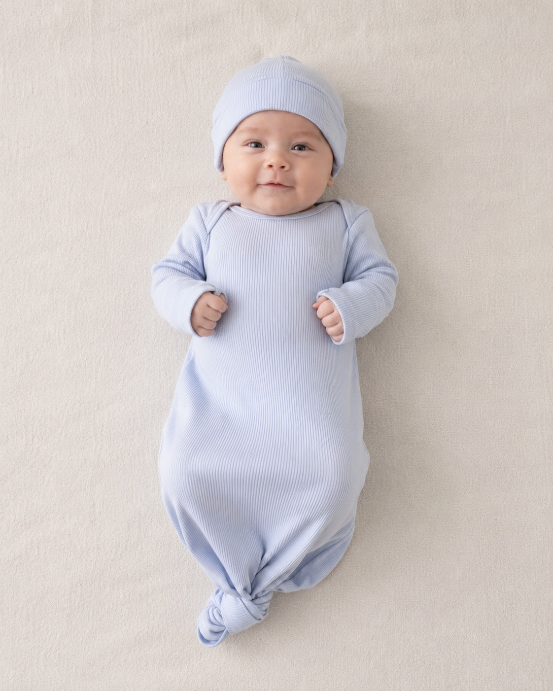Baby in a light blue outfit and hat lying on a beige surface