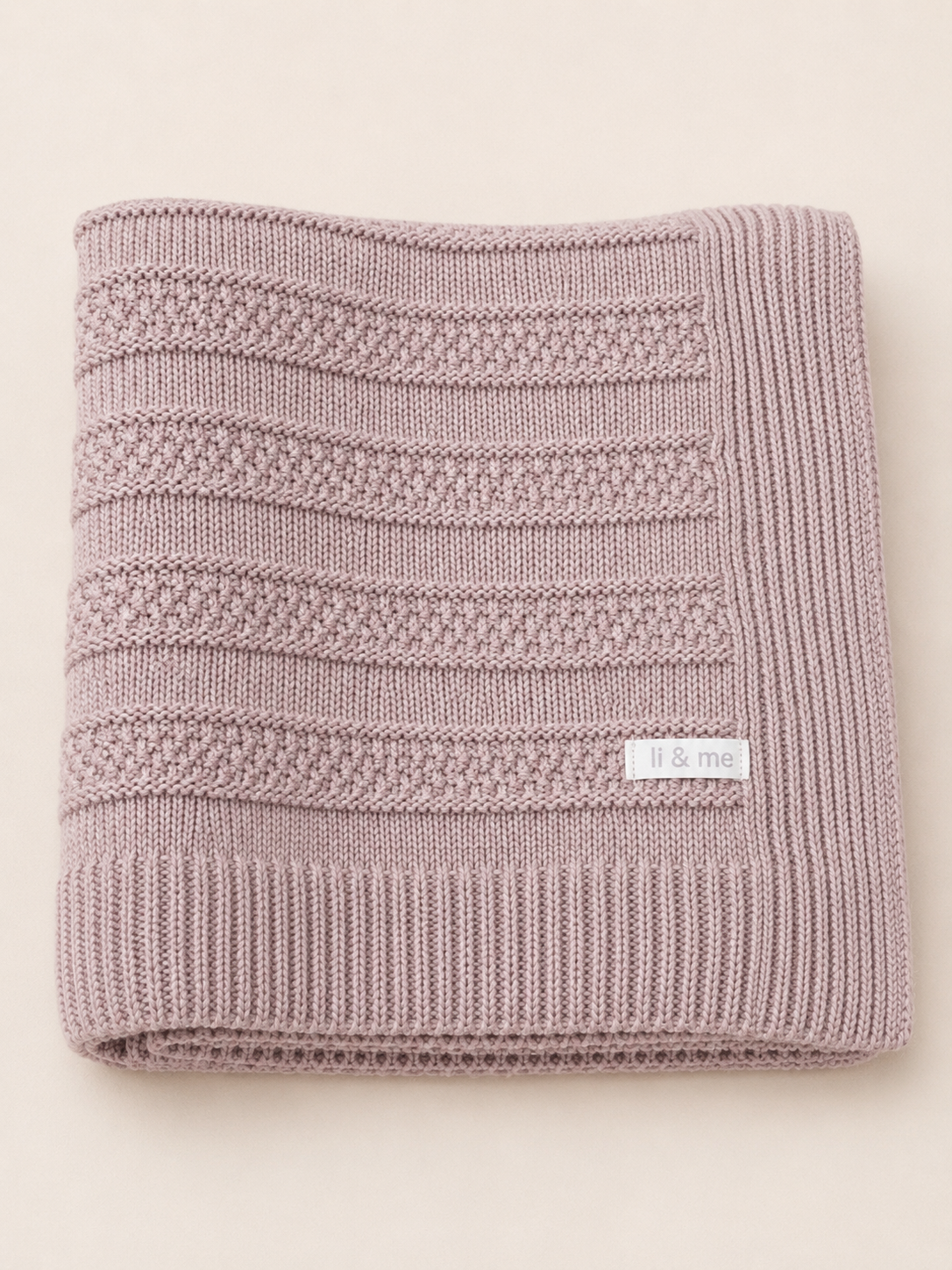 Knitted pink blanket with a brand label on a light beige background