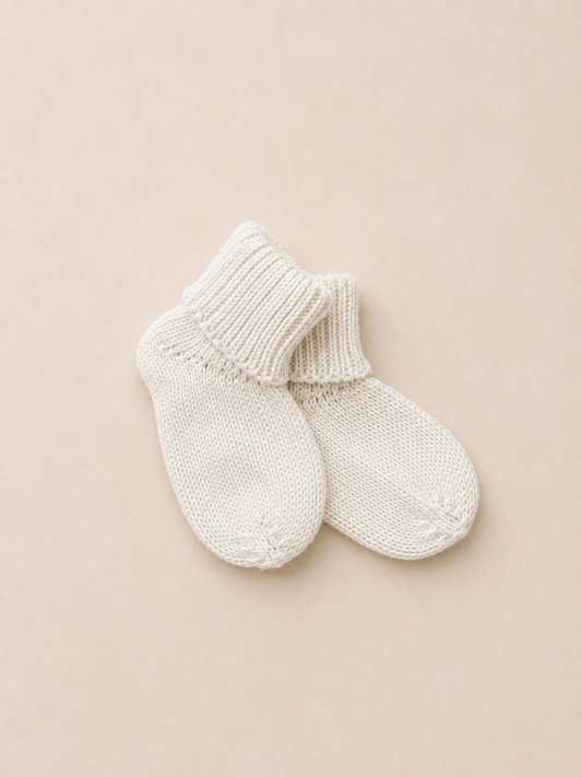 Pair of cream knitted socks on a beige background made from organic cotton