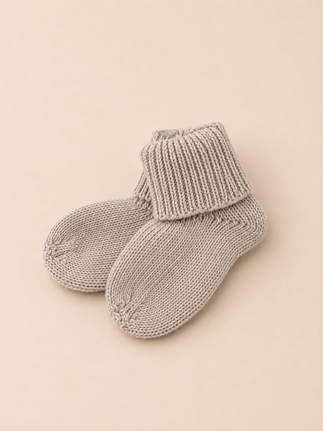 Pair of gray knitted baby socks on a beige background