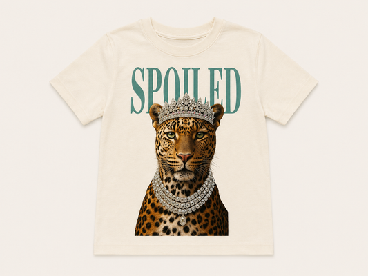 An off-white short-sleeve t-shirt featuring a graphic print of a leopard wearing a silver crown and diamond necklace, with the word 'SPOILED' printed in teal above it, set against a light beige background.
