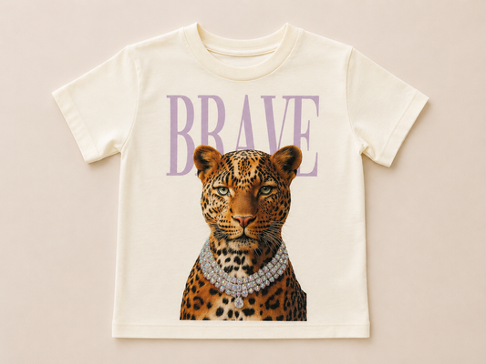 An off-white short-sleeve baby tee featuring a graphic print of a leopard wearing a diamond necklace under the word 'BRAVE' in lavender purple letters, displayed flat against a light beige background.
