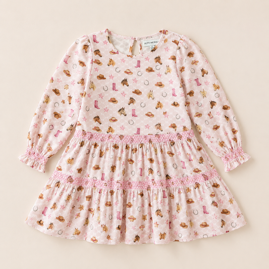 A long-sleeve girls dress with an allover cowboy and western-themed print, featuring brown boots, hats, horseshoes, and stars. The dress has a smocked waist, elasticized cuffs, and a tiered skirt