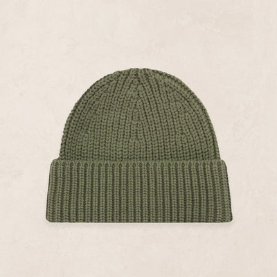 An olive green ribbed knit beanie hat, displayed flat against a light beige textured background.